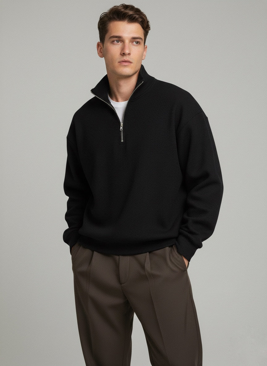 Man wearing a black quarter-zip sweatshirt and brown pants on a gray background