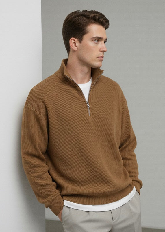 Man wearing a brown sweater with a zipper, white shirt, and beige pants against a plain background