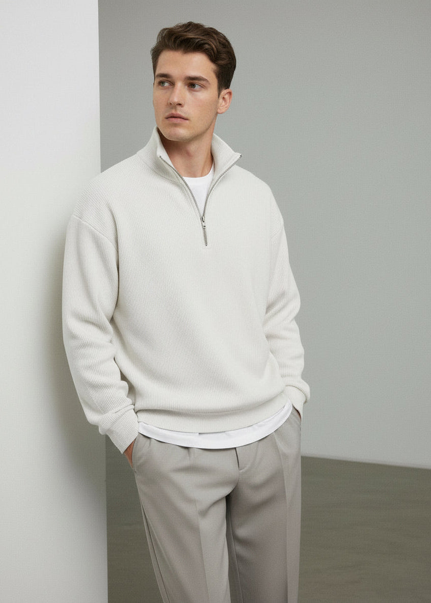 Man wearing a white half-zip sweatshirt and light gray pants against a plain background