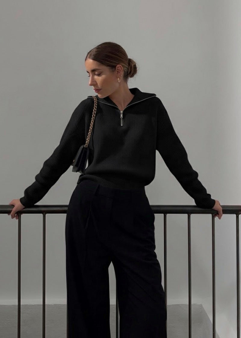 Woman in a black outfit standing against a plain background